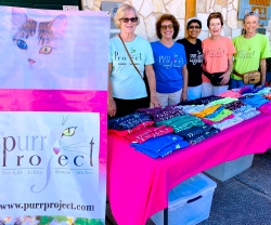 PuRR volunteers posing behind a table with a pink tablecloth and PuRR items for sale