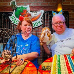 A couple posing with a stuffed animal kitty and calling the bingo numbers