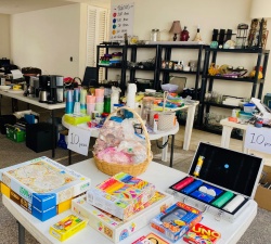 All sorts of items on a table and on shelves in a garage for a sale. 