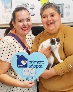 Two ladies holding a black and white kitty and a blue heart sign, saying they adopted him