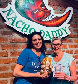 Two women posing in front of the Nacho Daddy Sign with the winnings from Bingo